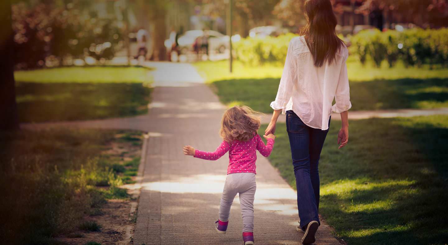A woman walks down a sidewalk with her daughter in hand.